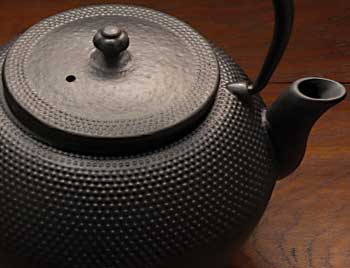 A black tea pot sitting on top of a wooden table.