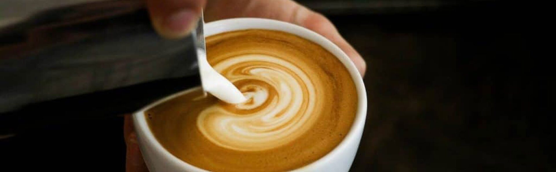 A person is pouring liquid into a cup of coffee.